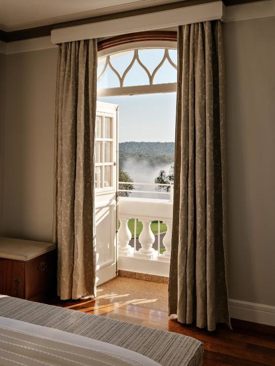 An open balcony door in a guest room looking out over the park at first light