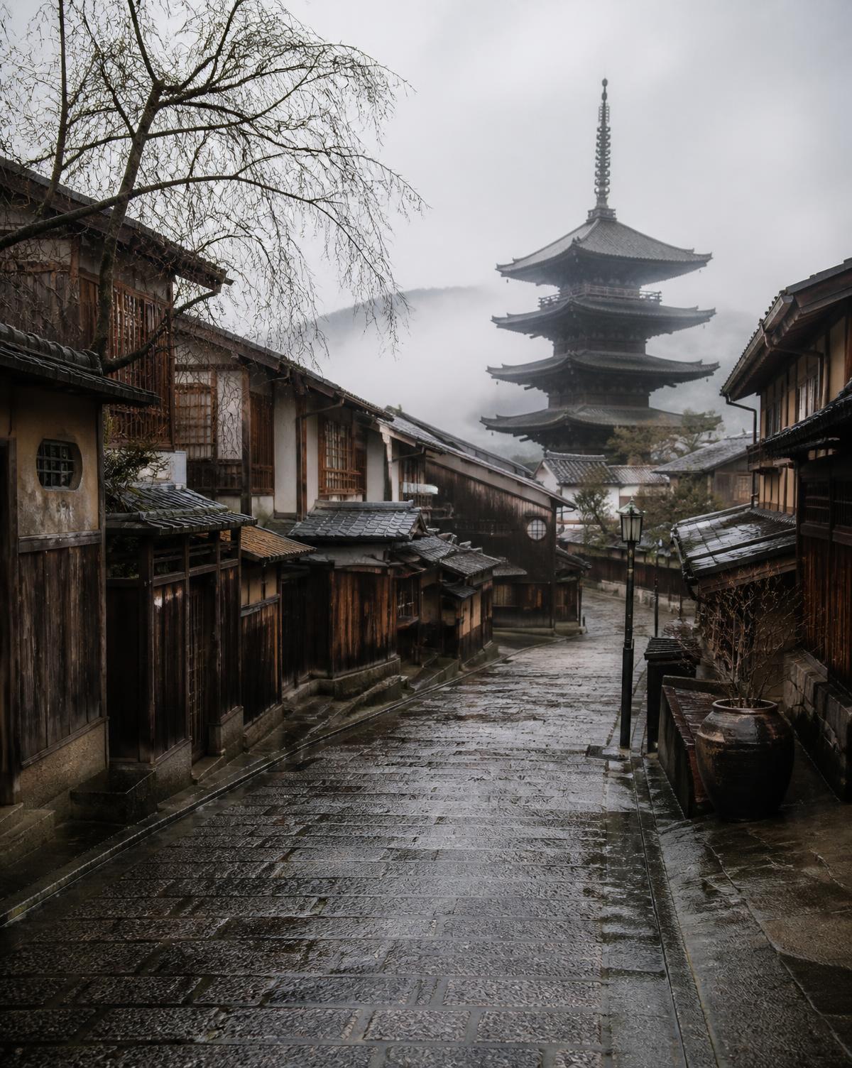 A quiet temple lane in Kyoto at dawn, wet stone and wooden facades in soft mist
